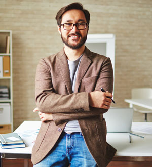 Smiling man with glasses and beard crossing arms in a cozy office.