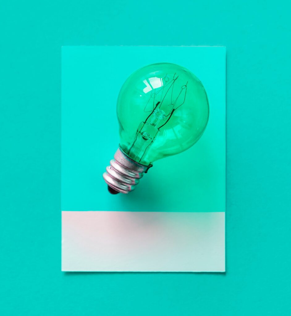A green light bulb resting on a blank white card against a turquoise background.