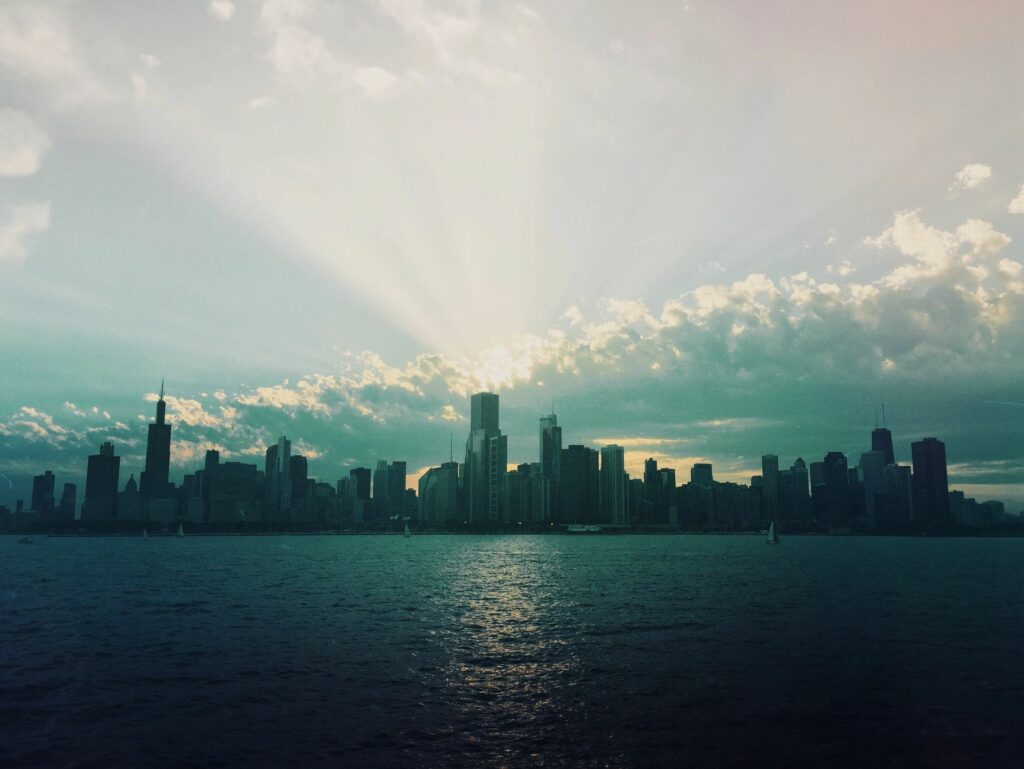 City skyline at sunset with dramatic clouds and rays over water.