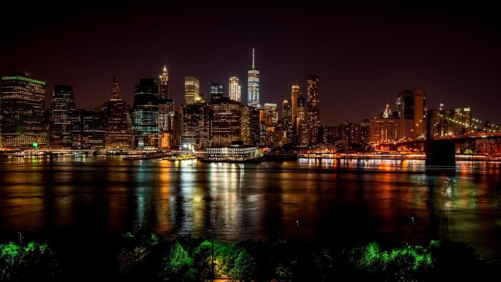 Nighttime city skyline with illuminated buildings reflecting on water.